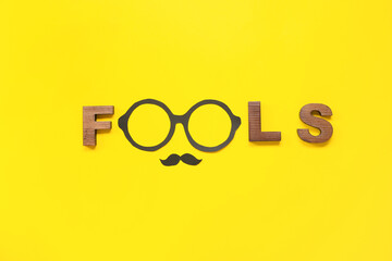 Word FOOLS and party decor on yellow background. April Fools Day celebration
