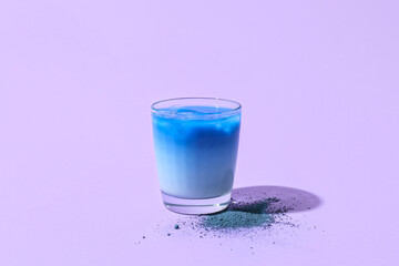 Glass of blue matcha tea and powder on purple background