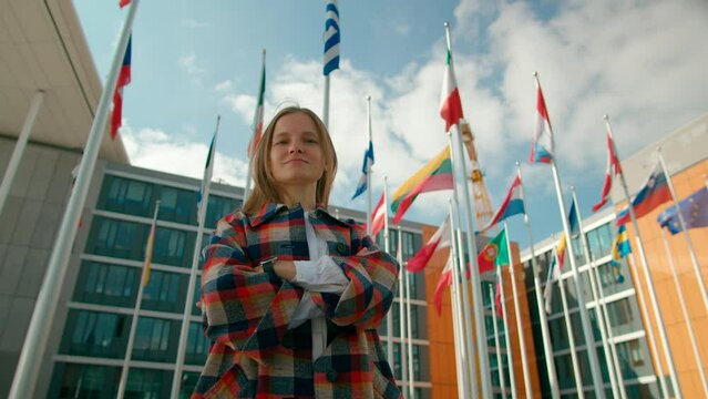 Portrait of Young Woman with Waving Flags of European Union Countries Outside of European Parliament administrative office in Luxembourg City. Politics, Migration and Citizenship concept. 4K hero shot