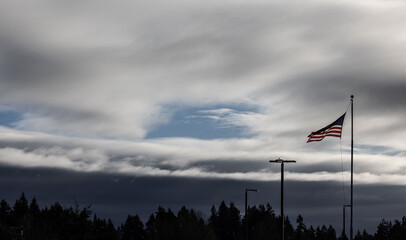 Fototapeta na wymiar An American flag blows in the wind off in the distance with beautiful clouds overhead and dark clouds below.