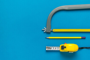 Hand hacksaw, tape measure and pencil on a blue background. A set of tools. Flat lay.