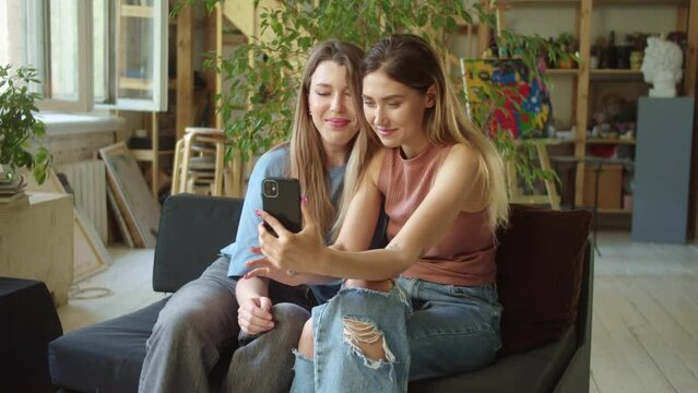 Two young lgbt ladies finish talking to their friends on the video call, they waving hands and sending a kiss