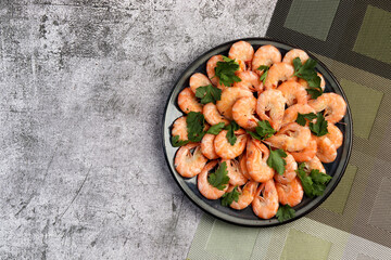 Boiled shrimps with parsley on a round plate on a dark gray background. Top view, flat lay