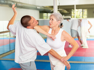 Fototapeta Senior woman exercising elbow strike on man during self-protection training. obraz