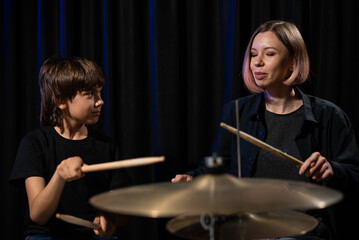 Young caucasian woman teaches a boy to play the drums in the studio on a black background. Music school student