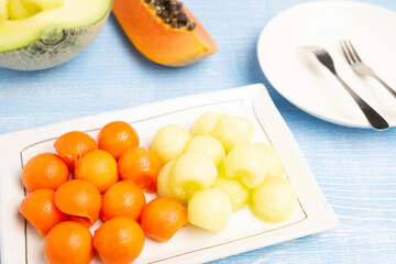 Organic Fresh Ripe Papaya, Thai tropical fruit and Fresh Japanese Melon cut in circle shapes serving on a white plate with blurred background of both types of fruits cut in pieces.	
