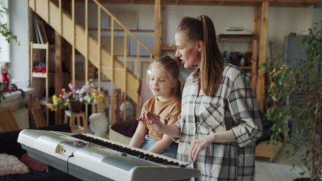 A woman shows the girl the basics of singing and uses the piano