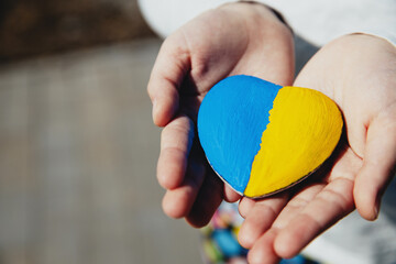 Small little kid hold heart shaped stone with Ukraine blue-yellow national flag or anthem. Girl...