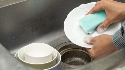 洗剤をつけたスポンジで食器を洗う