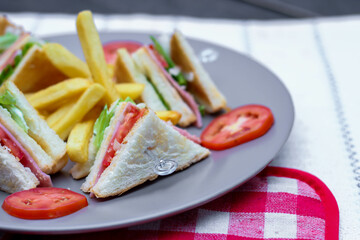 4 club sandwich slices laid out on a gray plate with tomatoes and fries.