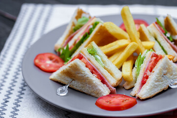 4 club sandwich slices laid out on a gray plate with tomatoes and fries.
