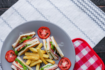 4 club sandwich slices laid out on a gray plate with tomatoes and fries.