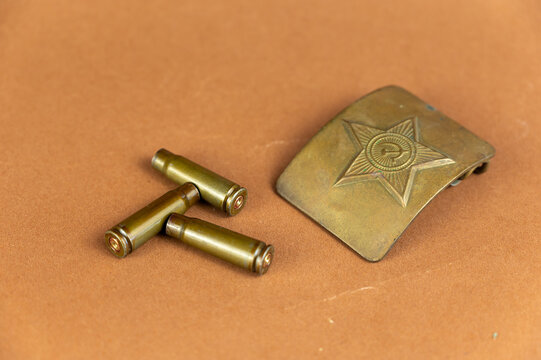Soviet belt buckle and empty shell casings against brown background. Attribute of the Red Army soldier's military clothing. Three automatic rifle casings.