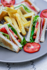 4 club sandwich slices laid out on a gray plate with tomatoes and fries.
