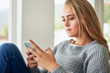 Fototapeta premium Sending some texts to her friends. Cropped shot of an attractive young woman sending a text message while chilling at home.