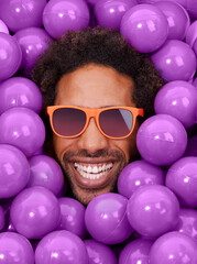 Looking cool and crazy. A young black mans face amongst purple pit balls.