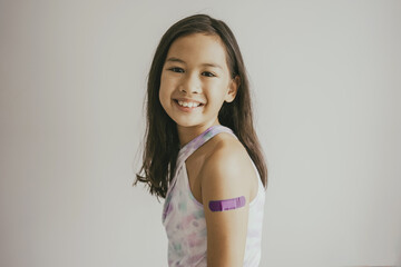 Mixed Asian preteen girl showing her arm with bandage after got vaccinated or inoculation, child...