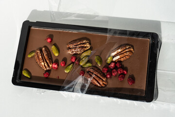 Close up shot of a chocolate bar with cranberries, hazelnuts and pistachio on a white background.  Nuts and berries in chocolate bars, slices and slices. 