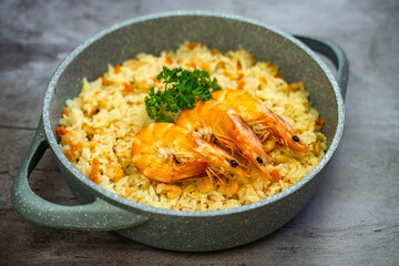 Rice with shrimps in a frying pan on a wooden table.