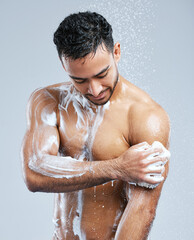 Lather up and scrub. Studio shot of a handsome young man taking a shower against a grey background.