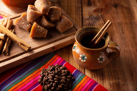 Cafe de Olla. Traditional Mexican coffee and basic ingredients for its preparation, coffee, cinnamon and piloncillo, served in a clay cup called "jarrito" on a rustic wooden surface.