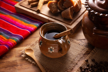 Cafe de Olla. Traditional Mexican coffee and basic ingredients for its preparation, coffee, cinnamon and piloncillo, served in a clay cup called "jarrito" on a rustic wooden surface.