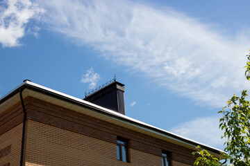 A roof with a chimney on the background of a blue summer sky.