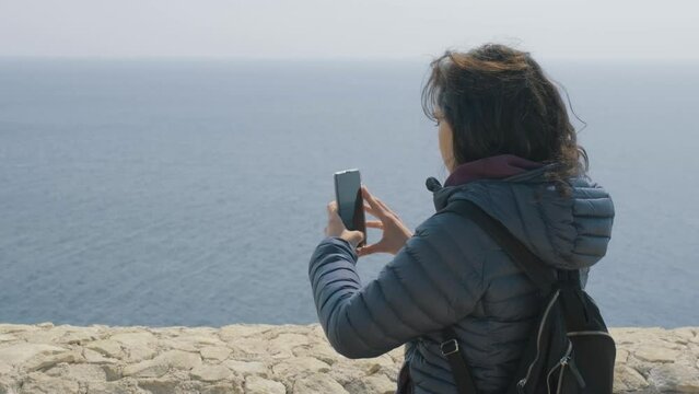 Young woman filming with her smart phone in front of the see during an outdoor expedition