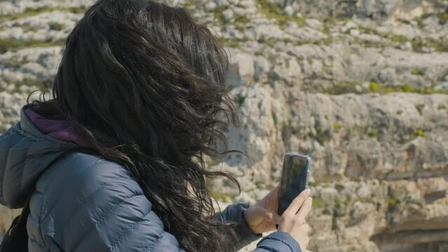 Young woman filming with her smart phone during an outdoor adventure with rocky landscape in the background