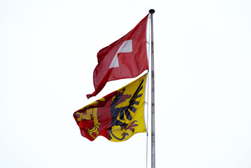 Flag of City of Geneva and Canton Geneva and Swiss flag waving on a cloudy and windy spring day. Photo taken March 18th, 2022, Geneva, Switzerland.