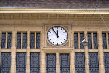 Clock at stone facade of railways station at City of Lausanne at five to twelve noon on a cloudy...