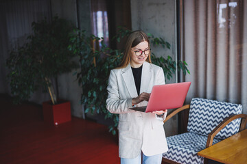 Female administrative manager in glasses and formal suit walking to office with digital laptop to check office workflow, confident female business owner
