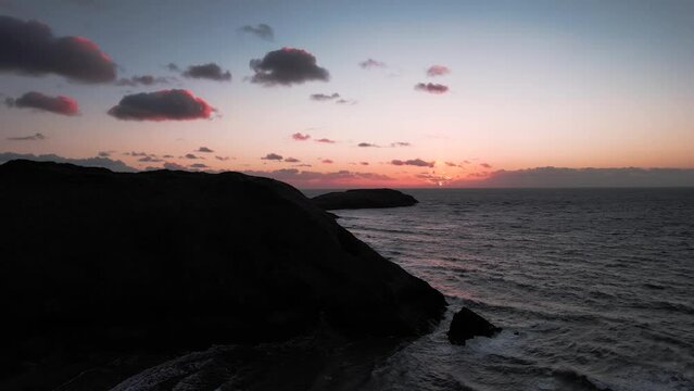 AERIAL: Silhouette reveal of rocky coastline and pink clouds, Bluepool Gower, 4k Drone