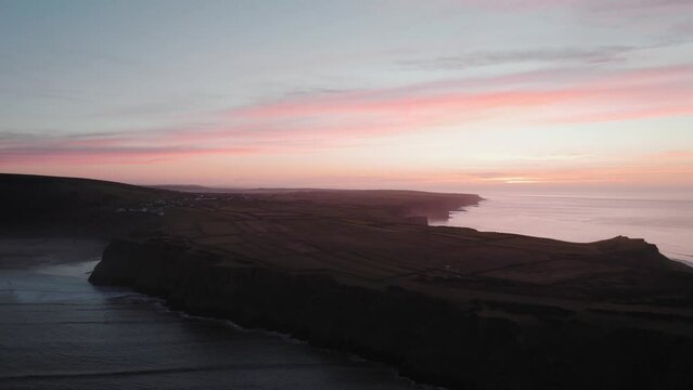 AERIAL: Ascending shot over coastline with pink sunset backdrop, Rhossili Gower, 4k Drone
