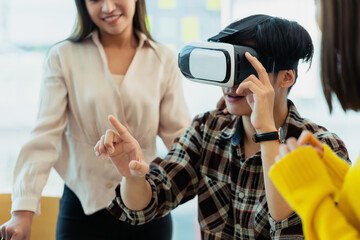 Group of young Asian business people using virtual reality glasses during meeting testing virtual...