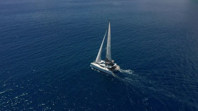 Aerial footage, rear view of luxury sailboat sailing on a deep blue sea with white wakes. Camera follow catamaran in blue ocean water