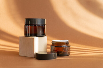 Two jars of amber glass for cosmetics on brown background in rays of sunlight. Mock-ups of...