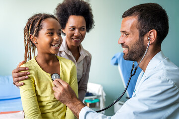 Pediatrician examining a little african girl at hospital. Healthcare, people concept