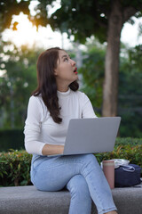 Cute young Asian female student working on a laptop computer outdoors, studying concepts, working in the public domain.
