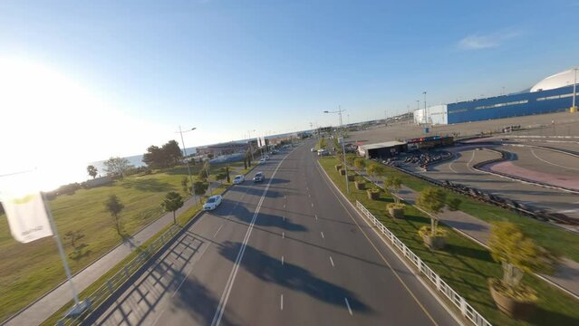 Aerial view sports FPV drone flying over resort touristic neighborhood with highway palm trees clear blue sky mountains and sea embankment. Shooting from helicopter amazing summer urban scenery