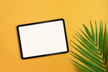 Mockup digital tablet and tropical palm leaves on yellow background. Summer vacation concept.