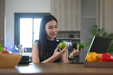 Millennial woman looking online recipe on digital tablet while preparing healthy meal at home kitchen.