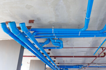 Red fire water pipes on the concrete wall in the condo building.Installation of drainage pipes in...