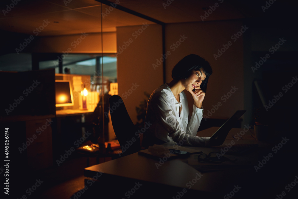 Poster getting it done after dark. shot of a young businesswoman using a digital tablet during a late night