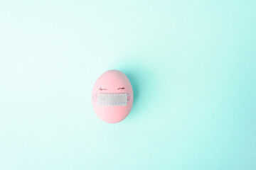 One pink colorful Easter egg with painted eyes and with protective mask covid-19. Happy Easter holidays. The concept of celebrating Easter on quarantine