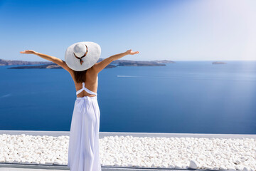 Travel to Greece concept with a woman in a white dress looking at the blue, Aegean sea at Santorini...