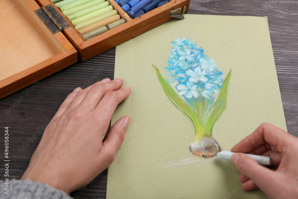 Poster Woman drawing blue blooming hyacinth on paper with soft pastels at wooden table, closeup