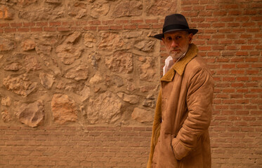 Portrait of adult man in hat and coat against brick wall on street. Madrid, Spain