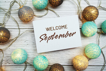 Welcome September text on paper card with LED cotton balls top view on wooden background - obrazy, fototapety, plakaty