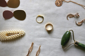 Various gold jewelry, personal accessories and beauty products on neutral background. Flat lay.